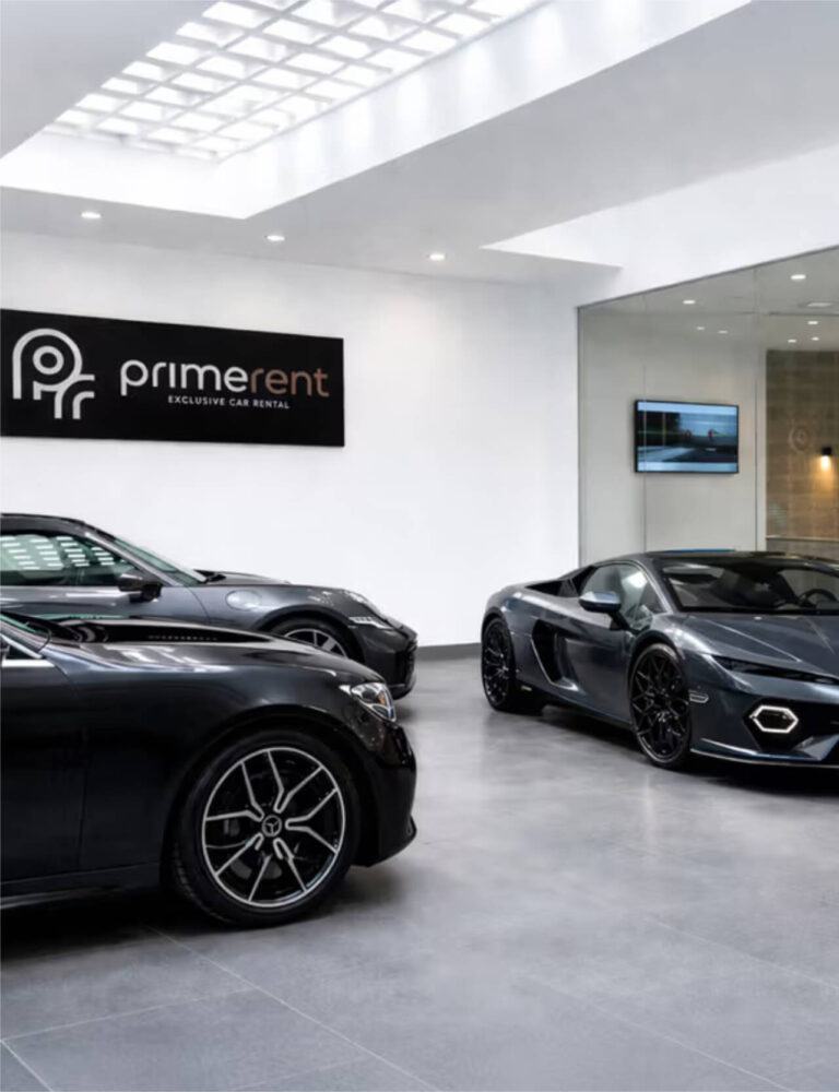 Showroom di autonoleggio di lusso con insegna "Primerent - Exclusive Car Rental" e due auto sportive nere in primo piano.