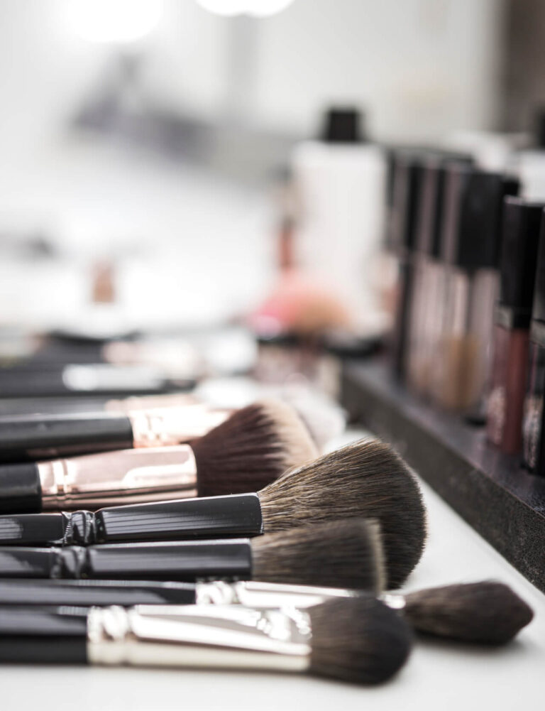 Primo piano di pennelli da make-up professionali disposti su un piano, con prodotti cosmetici sfocati sullo sfondo.
