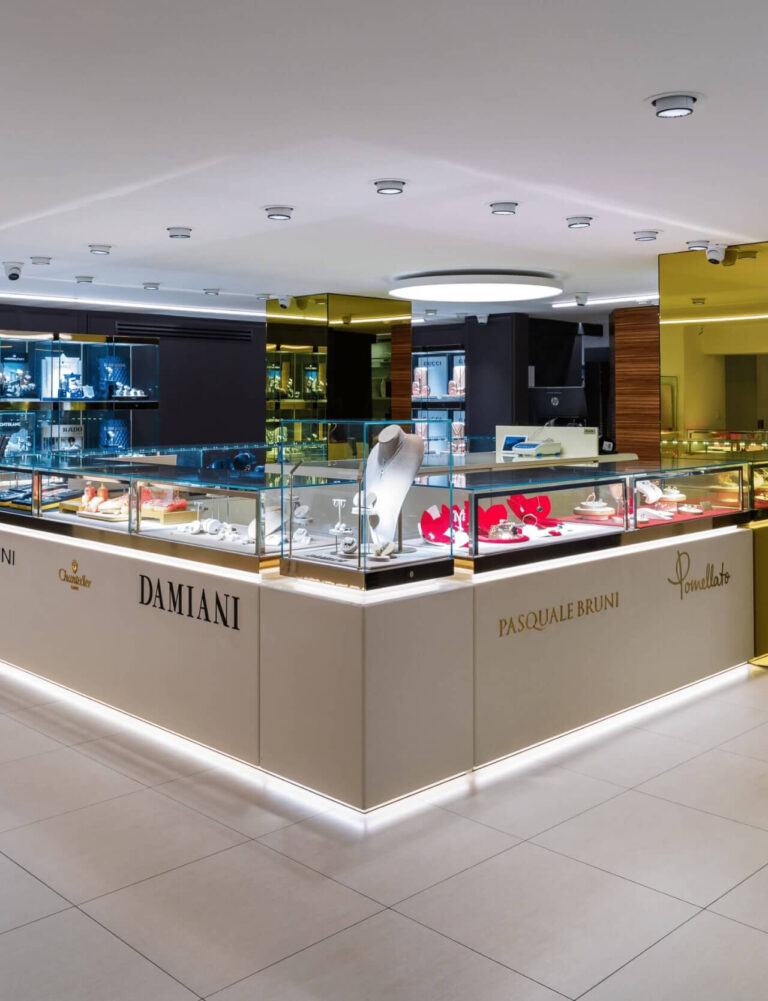 Interno di una gioielleria con vetrine espositive illuminate e insegne dei marchi Damiani, Pasquale Bruni e Pomellato.